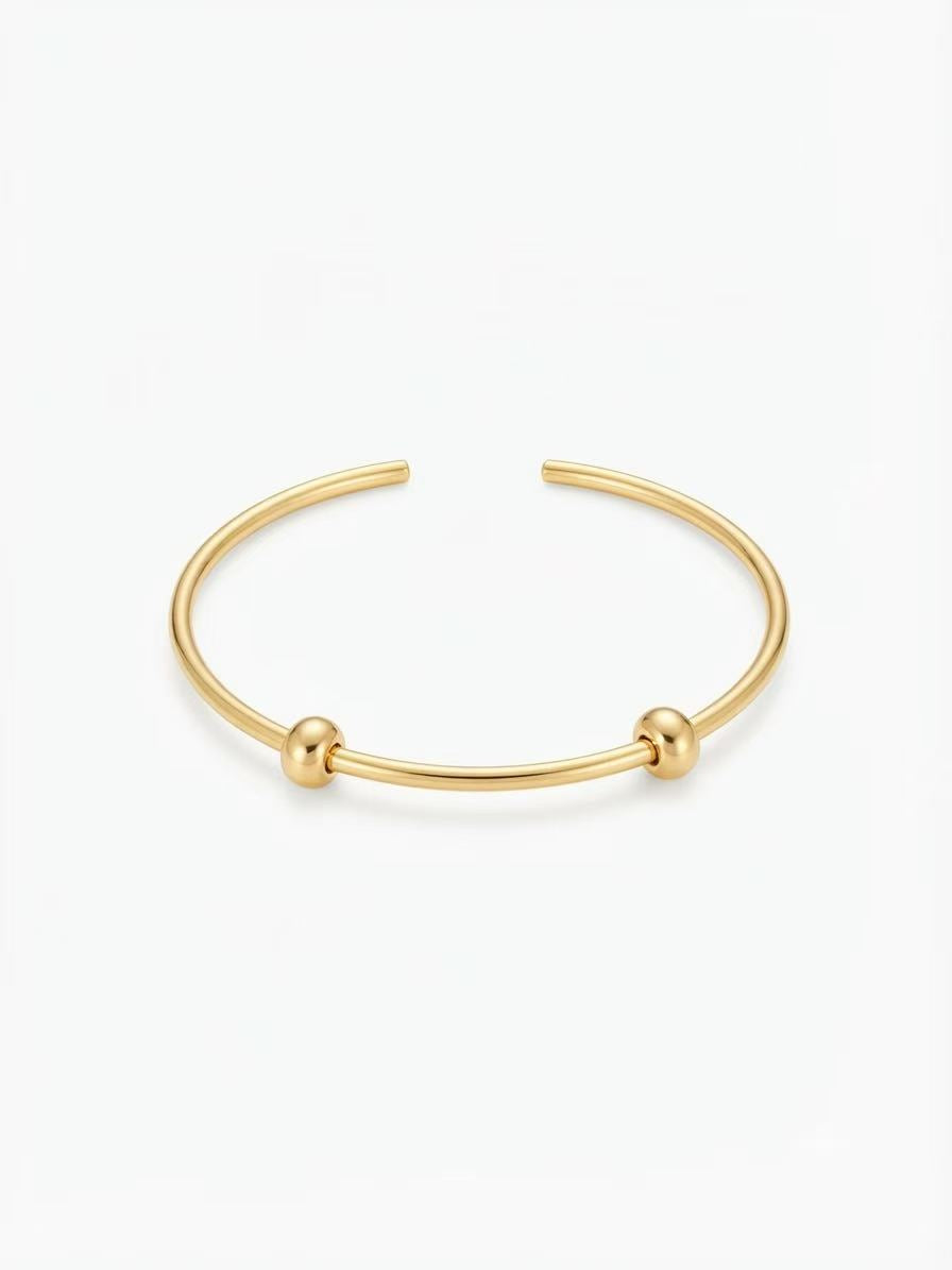 Waterproof gold-plated open charm bangle with two silicone-lined stopper beads on a white background